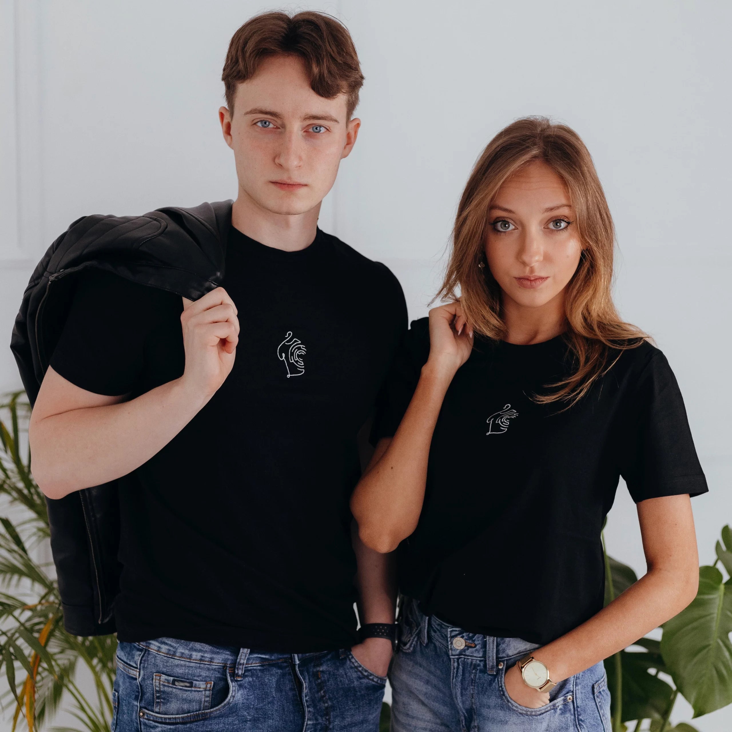 Kobieta i mężczyzna w jeansach prezentują dopasowany black minimaze t-shirt z minimalistycznym, linearnym haftem na piersi.