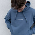 Mężczyzna z głową skierowaną w dół, prezentujący niebieską bluzę z kapturem oraz białym napisem na piersi, czyli oryginalny blue minimaze hoodie.