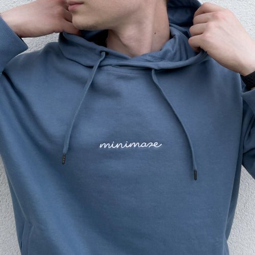 Zbliżenie na profil mężczyzny w niebieskiej bluzie z kapturem, prezentujące biały napis na klatce piersiowej oryginalnego blue minimaze hoodie.