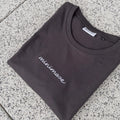 Grafitowy t-shirt rozłożony na szarych płytkach, prezentujący minimalistyczny graphite minimaze t-shirt z białym, odręcznym napisem z przodu.
