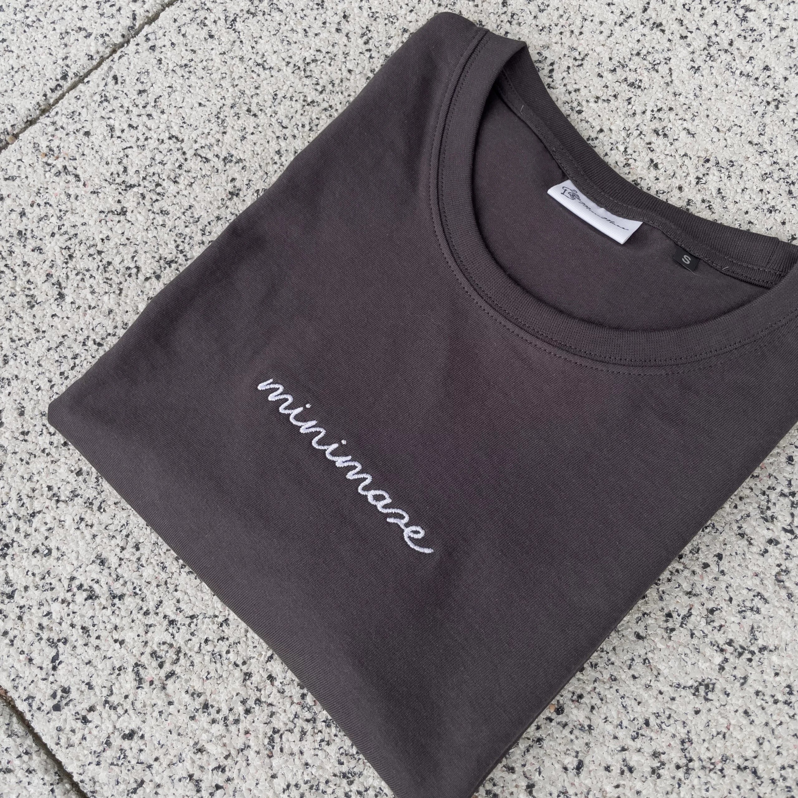 Grafitowy t-shirt rozłożony na szarych płytkach, prezentujący minimalistyczny graphite minimaze t-shirt z białym, odręcznym napisem z przodu.