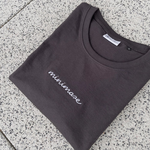 Grafitowy t-shirt rozłożony na szarych płytkach, prezentujący minimalistyczny graphite minimaze t-shirt z białym, odręcznym napisem z przodu.