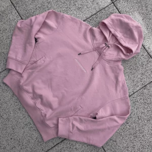 Różowa bluza z kapturem marki minimaze, wykonana z miękkiego materiału, z minimalistycznym napisem 'minimaze' na klatce piersiowej. Bluza posiada kieszenie typu kangurka oraz regulowany kaptur, idealna na chłodniejsze dni.