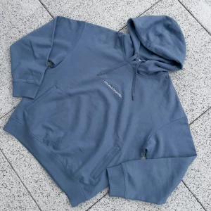 Niebieska bluza z kapturem marki minimaze, wykonana z miękkiego materiału, z minimalistycznym napisem 'minimaze' na klatce piersiowej. Bluza posiada kieszenie typu kangurka oraz regulowany kaptur, idealna na chłodniejsze dni.